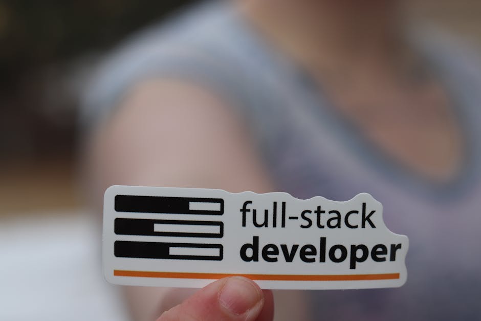 A close-up view of a hand holding a rectangular sticker with a white background. The sticker displays three black horizontal lines resembling a computer code or programming symbol, followed by the tex